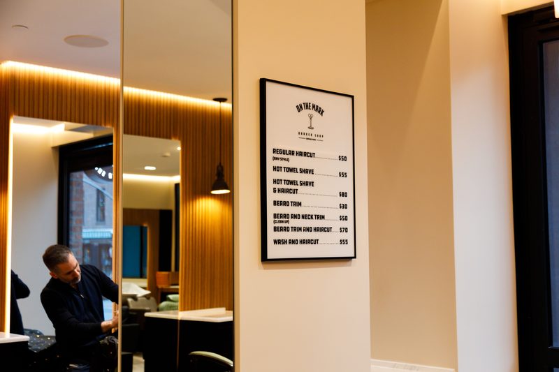 The price board on the shop wall, a barber at work in the mirror